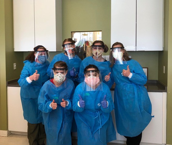 Group of female Baker Hughes employees wearing medical face shields and blue overall body protectors