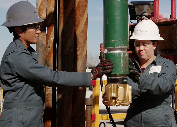 Two Baker Hughes employees installing a drill bit on an oil rig.
