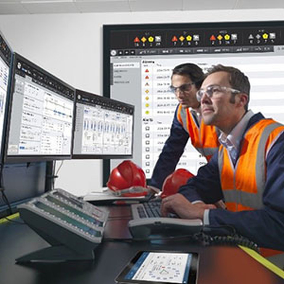 Two workers safety vests and protective glasses looking at multiple screens