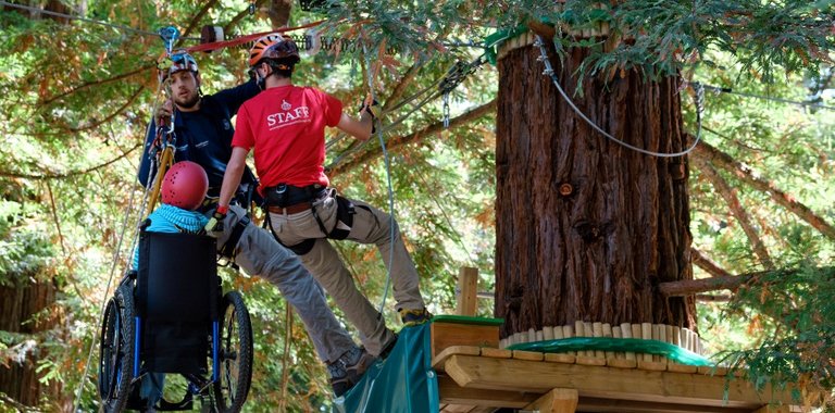 Dynamo Camp staff help child in wheelchair onto tree platform