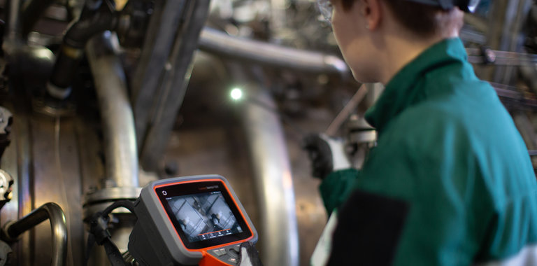 Technician in green suit uses Everest Mentor Flex video borescope to conduct inspection.